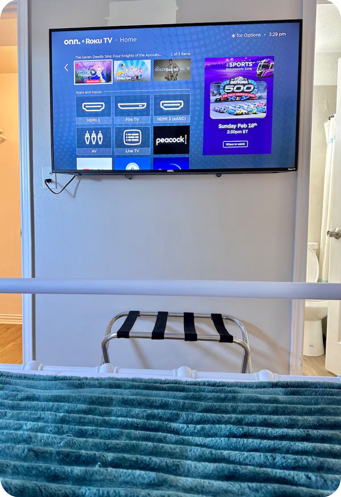 A television mounted on a wall displaying a Roku TV interface with various streaming options and a sports event advertisement.