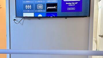 A television mounted on a wall displaying a Roku TV interface with various streaming options and a sports event advertisement.