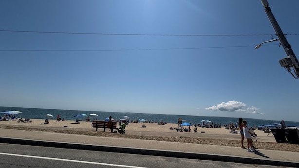 Een strand met mensen, parasols en een heldere lucht.
