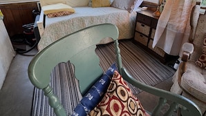 Een gezellige kamer met een bed, een stoel, een klein tafeltje met een lamp en een raam met gordijnen.