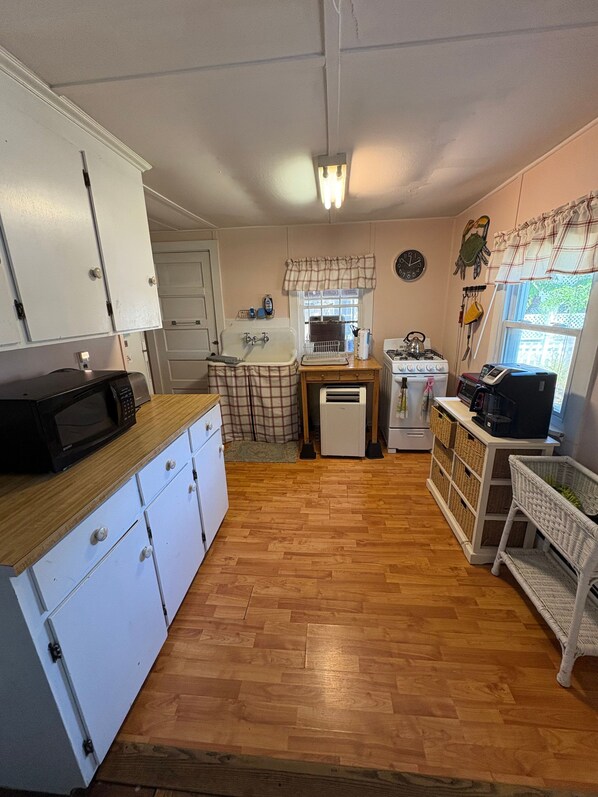 A compact kitchen with white cabinets, a microwave, a sink, and a stove.