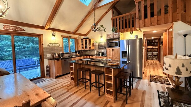 A spacious kitchen with wooden beams, a large island with stools, and a view through the glass doors.
