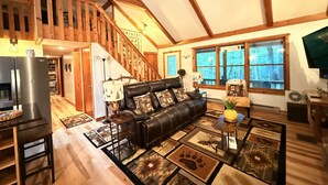 A spacious living room with a leather sofa, wooden flooring, and a staircase leading to an upper level.