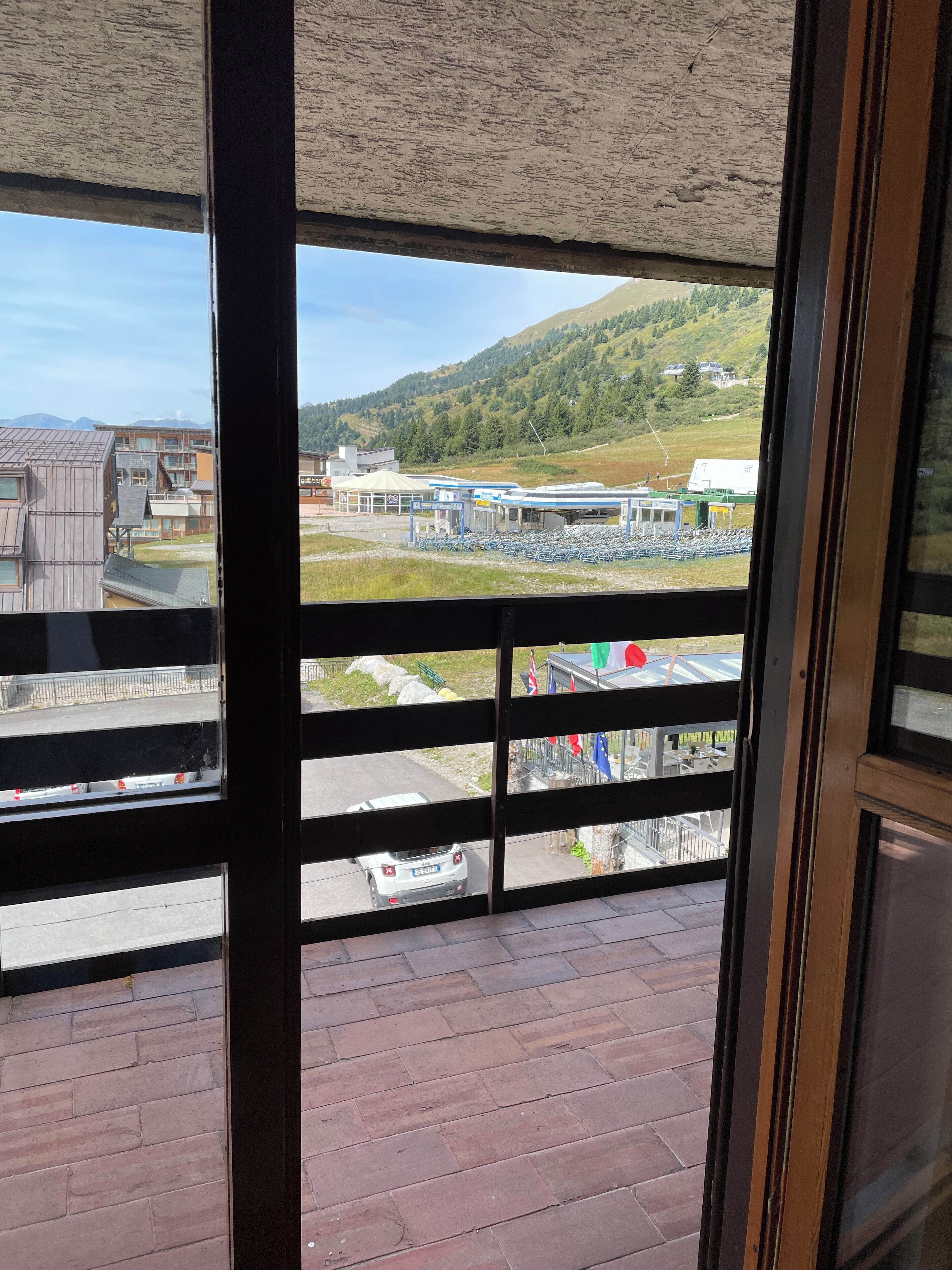 Vista dalla finestra su un complesso di edifici, comprensivo di area parcheggio e bandiere.