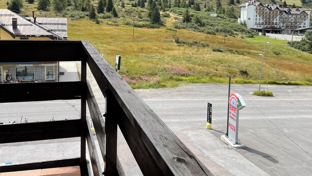 A mountain view from a balcony with a wooden railing, a paved area, and a sign for a bar and pizza restaurant.