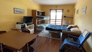 A compact living space with a bed, a TV, a dining table, and a kitchenette.