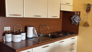 A kitchen with white cabinets, a wooden countertop, a stainless steel sink, and a stove. There are three white containers labeled "Caffè," "Biscegli," and "Chicco."
