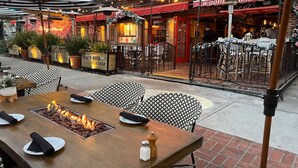 Un espace extérieur aménagé pour les repas, avec des tables et des chaises, un foyer et une enseigne indiquant le « Bernini's Bistro ».