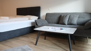 A modern room with a bed, a grey sofa, and a small table with magazines. - Comfort Apartments Villach Self CheckIn (Villach)