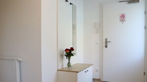 A hallway with a white radiator, a wooden counter with a vase of red roses, and a white door with a no-smoking sign. - Comfort Apartments Villach Self CheckIn (Villach)
