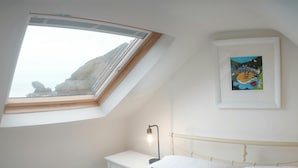 Een slaapkamer met dakraam, een bed met gestreepte kussens, een nachtkastje, een lamp en een ingelijst beeld aan de muur.