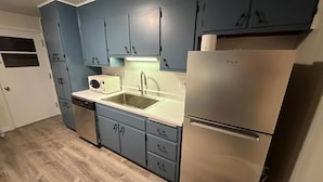 A compact kitchen with blue cabinets, a stainless steel refrigerator, a microwave, and a dishwasher. - Steps to Metra - Fully Updated - Downtown Harvard (Harvard)