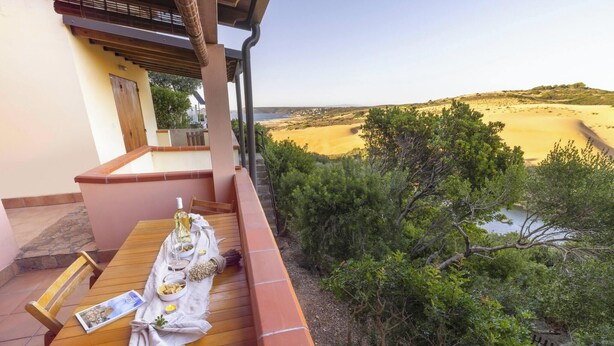 Un balcón con una mesa preparada para comer, con vista a una playa y vegetación.