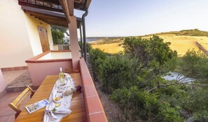 Un balcón con una mesa preparada para comer, con vista a una playa y vegetación.