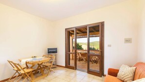 Una habitación con una mesa de comedor, sillas, un televisor y un ventanal corredero que da a un espacio exterior con vistas a las colinas.