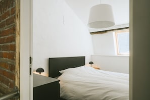 Un dormitorio con cama, mesita de noche, lámpara y ventana.