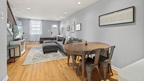 A modern living room with a grey sofa, a wooden dining table, and a staircase. - The Bella Vista Townhouse (Philadelphia)