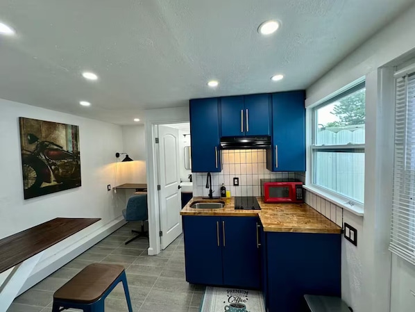 A compact kitchen with blue cabinets, a red microwave, and a wooden countertop.