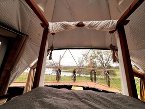 A tent with a bed, a view of the outdoors, and a hanging decoration.