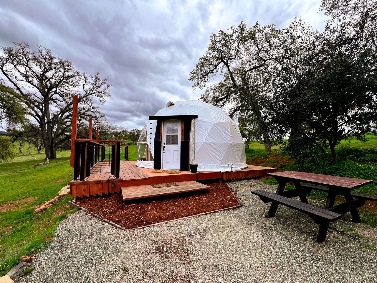 A small, dome-shaped tent with a door and windows, a wooden deck, and a picnic table.