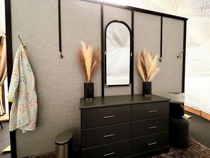 A room with a black dresser, a mirror, and pampas grass in vases.
