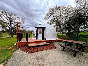 A small, dome-shaped tent with a door and windows, a wooden deck, and a picnic table. - Luxurious Rustic Dome with Private Deck and Picnic Table in California (Grass Valley)