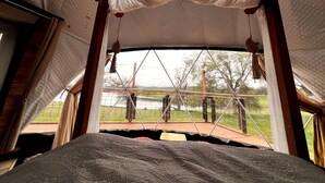 A tent with a bed, a view of the outdoors, and a hanging decoration.