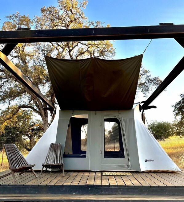 A tent with a canopy, a bench, and a wooden deck.