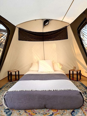 Une tente équipée d’un lit, d’oreillers, d’une couverture et de deux tables de chevet.