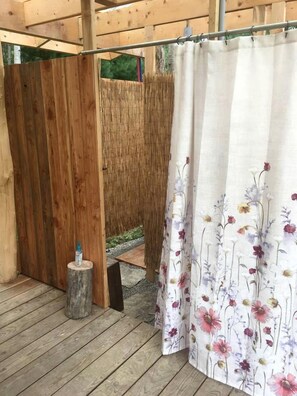Una terraza de madera con cercado de madera, un taburete pequeño de madera y una cortina de ducha con motivos florales.