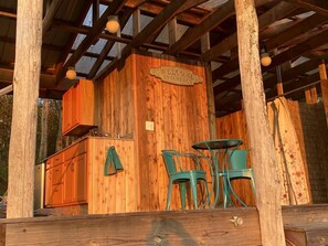 A rustic wooden structure with a 'Welcome to Our Farm' sign, a small kitchen area, and a seating arrangement with chairs.