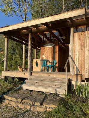 Une structure rustique en bois, dotée d’un porche, d’une pancarte de bienvenue et d’une table avec des chaises.