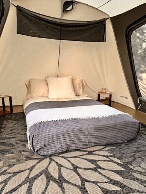 A tent with a bed, a window, and a small table with a lamp.