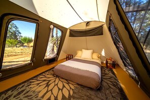 A tent with a bed, a small table, and a window.