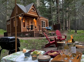 A wooden cabin with a porch, outdoor seating, a fire pit, and a table set for a meal.