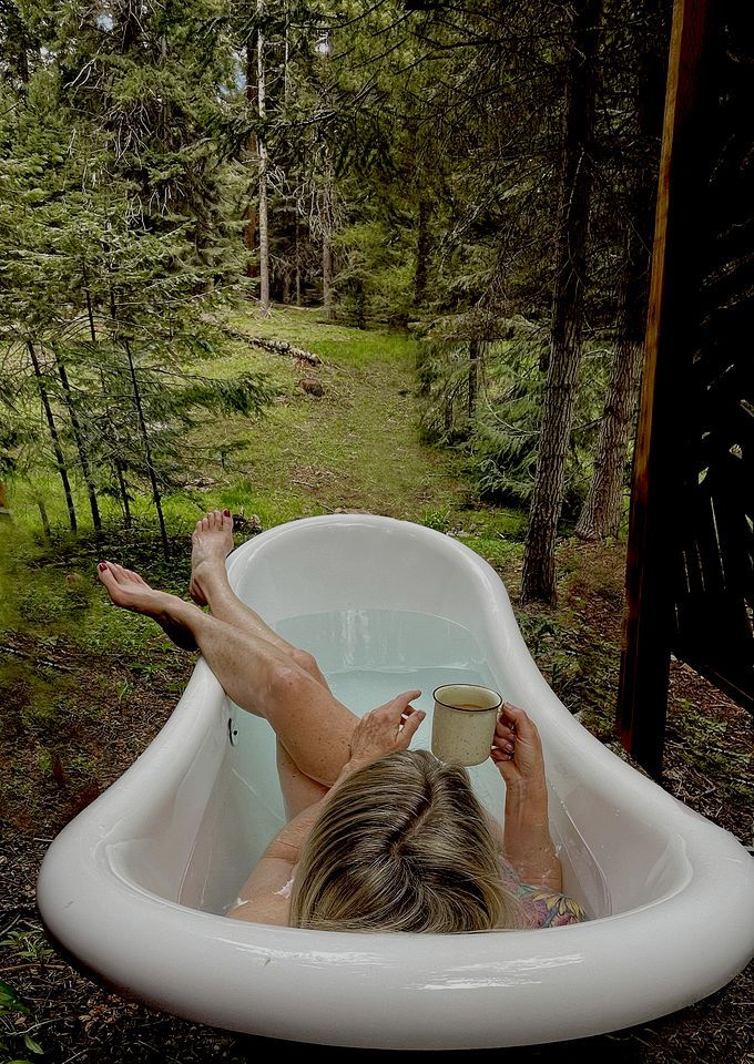 Una persona si rilassa in una vasca da bagno all'aperto, circondata da alberi.