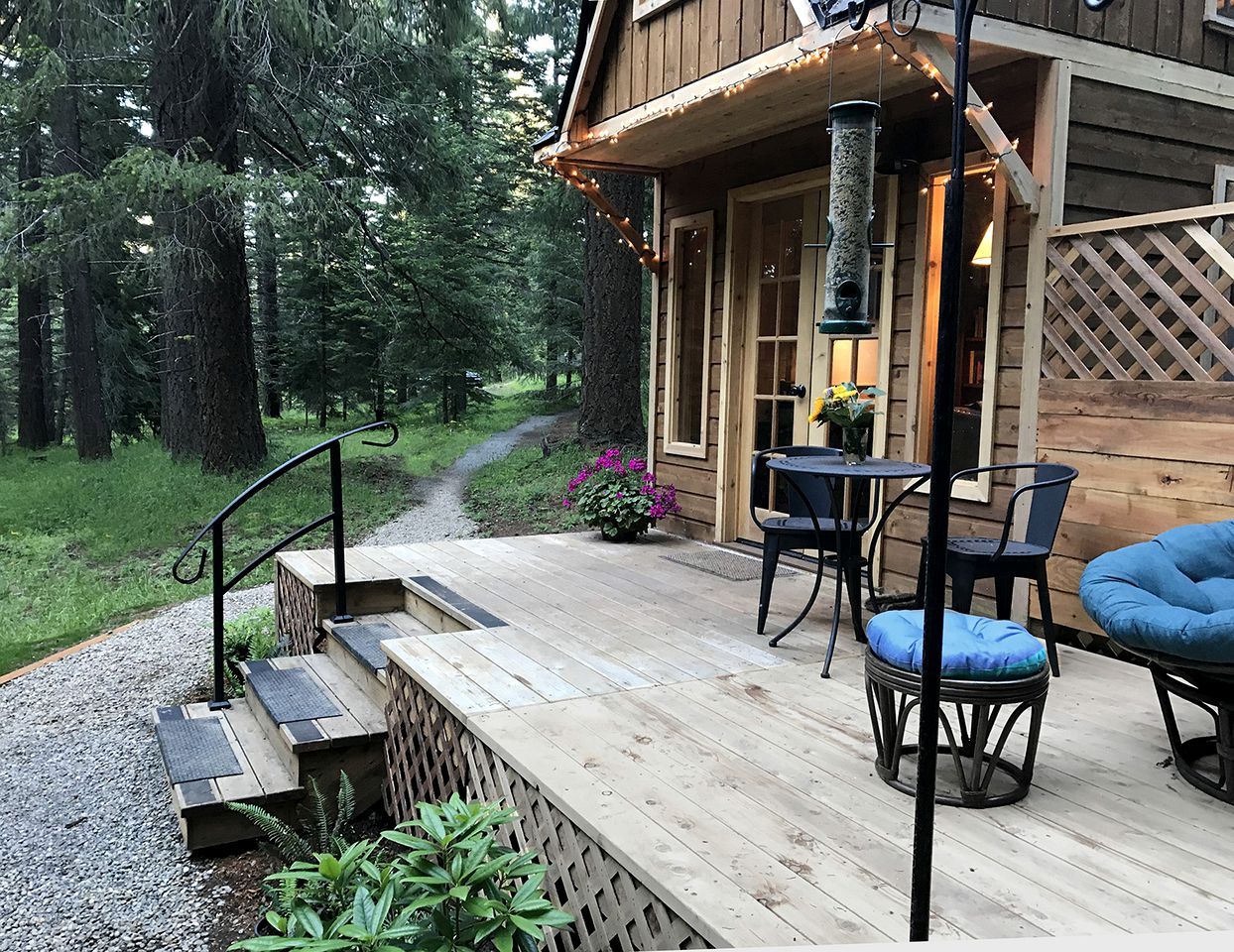 Una terraza de madera con asientos exteriores, una escalera y un sendero que lleva a un edificio.