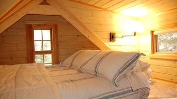 Une chambre mansardée chaleureuse, avec un plafond en pente, un lit avec une literie à rayures, une fenêtre et un luminaire fixé au mur.