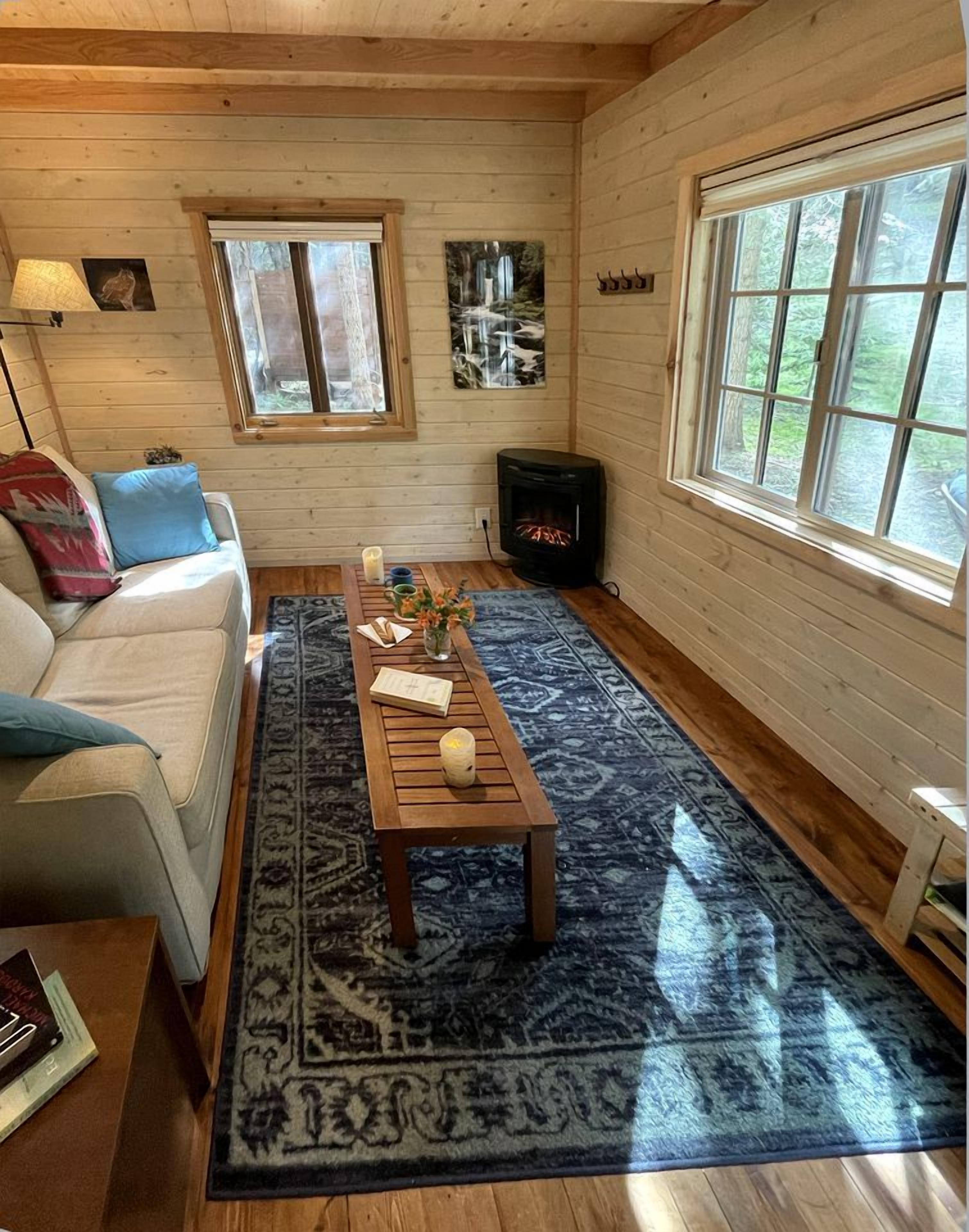 L’intérieur d’un chalet accueillant, avec un canapé, une table basse, une cheminée et une grande fenêtre.
