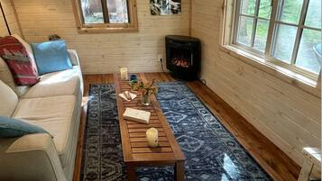 L’intérieur d’un chalet accueillant, avec un canapé, une table basse, une cheminée et une grande fenêtre.