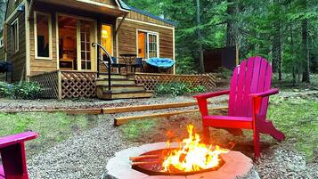 A wooden cabin with a porch, a fire pit, and outdoor seating.