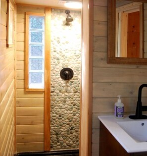 Een houten badkamer met een vakantiehuisje, een stenen muur, een raam, een douche en een wastafel met zeep.