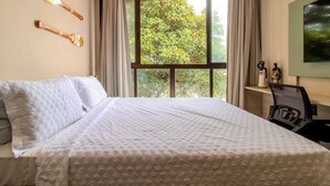 A hotel room with a large bed, a desk with a chair, a window with curtains, and wall-mounted decorative items. - Get Sense (João Pessoa)