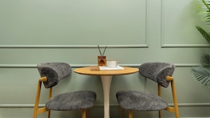 Deux fauteuils gris, recouverts de tissu, avec des pieds en bois, et une table ronde en bois dotée d’un pied central blanc.