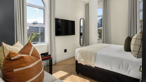 Une chambre d’hôtel moderne dotée d’un grand lit, d’une télévision à écran plat, d’un miroir et offrant une vue sur la ville.