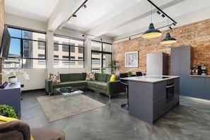 A modern living space with a green sofa, a glass coffee table, a kitchen area with a built-in island, and large windows offering views of the city. - New York Style apartment | Face Brick (Cape Town)