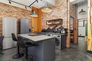 Een moderne keuken met een centraal eiland, barstoelen, een wasmachine en een bakstenen muur.
