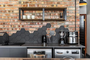 A kitchen with a brick wall, a coffee machine, a blender, and a dishwasher. - New York Style apartment | Face Brick (Cape Town)
