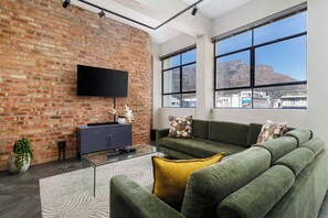 Een moderne woonkamer met een bakstenen muur, een flatscreen-televisie, een zithoek en uitzicht op een berg door grote ramen.