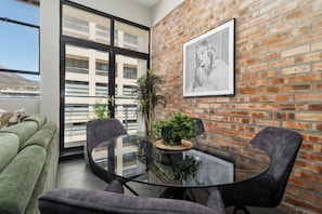 A modern living space with a glass table, two chairs, a green sofa, and a brick wall.